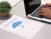 Close-up of hands typing on laptop with an insurance document visible on the desk.